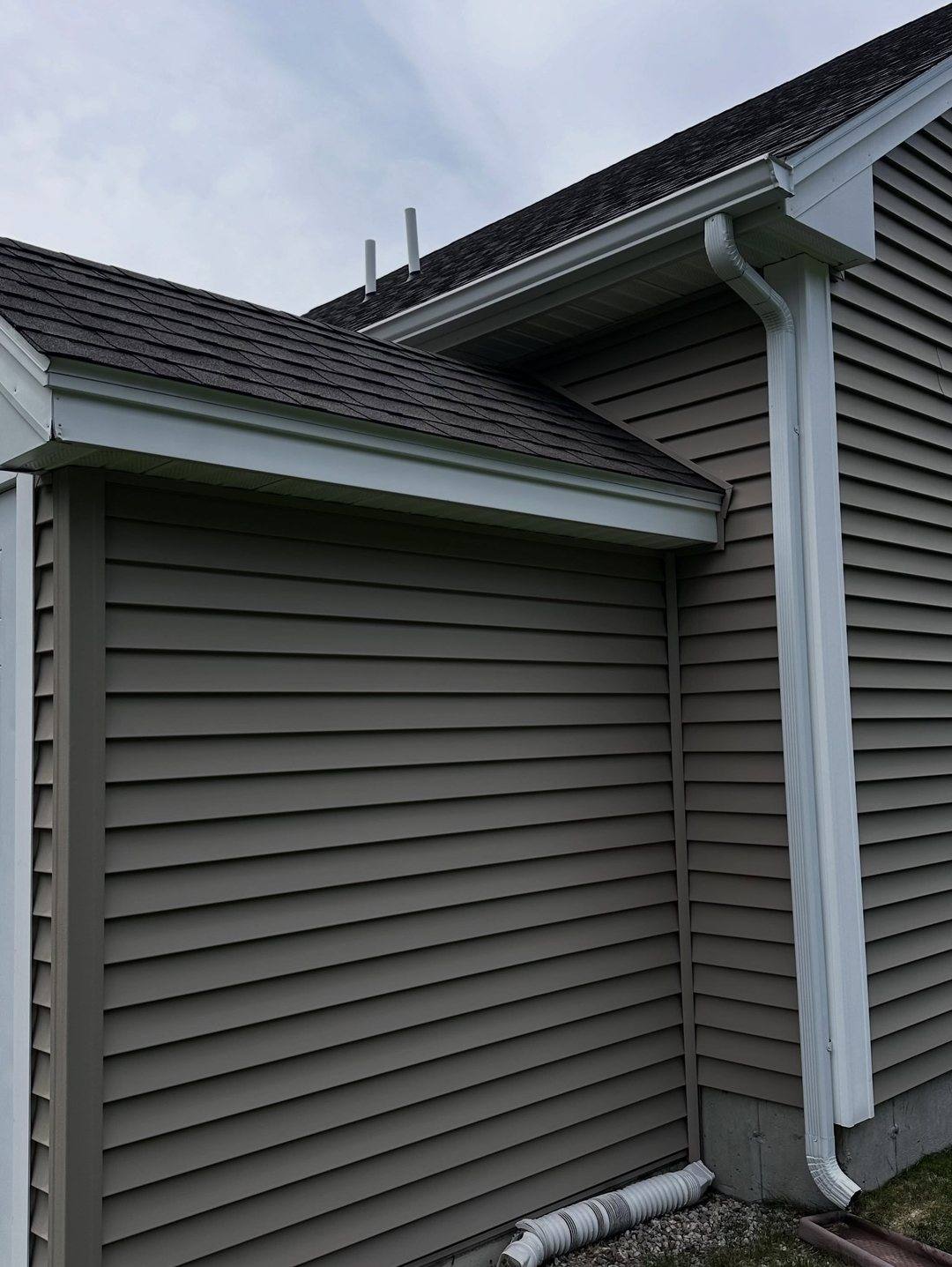 Taupe vinyl siding, white trim and a downspout after a full house soft wash